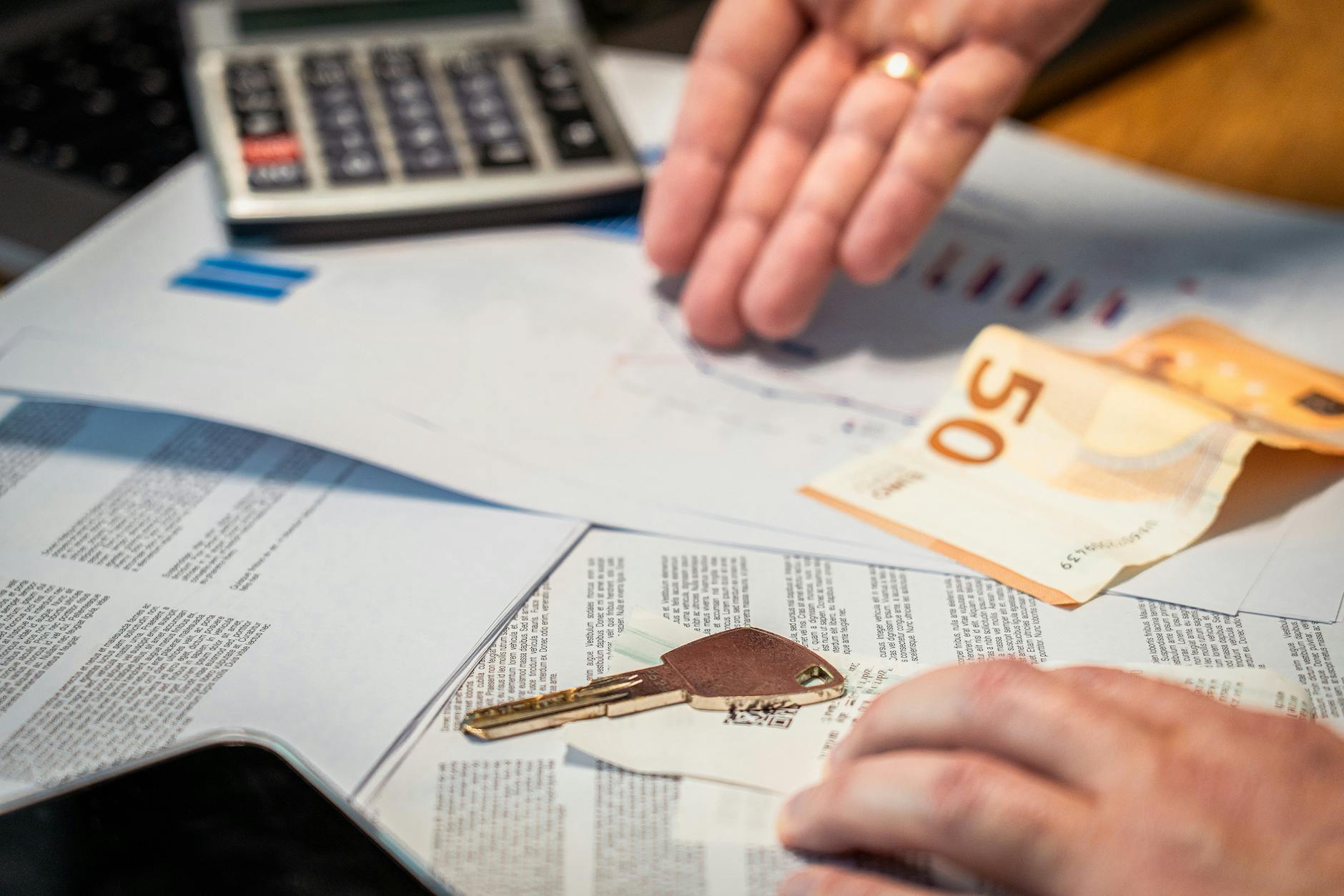 hands examining financial documents, a 50 euro note, and a key, suggesting investment or real estate themes showing protect assets from creditors strategy for high-net-worth